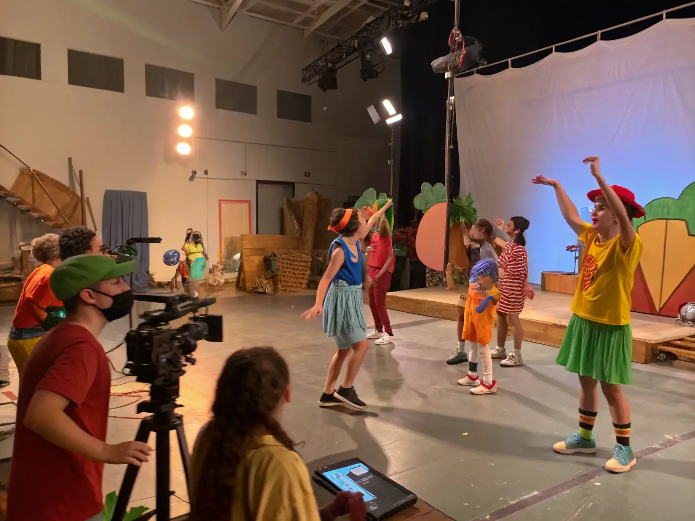 A diverse group of teenagers participating in a drama workshop, rehearsing a scene on a stage with colorful costumes and props. The atmosphere is energetic and collaborative.